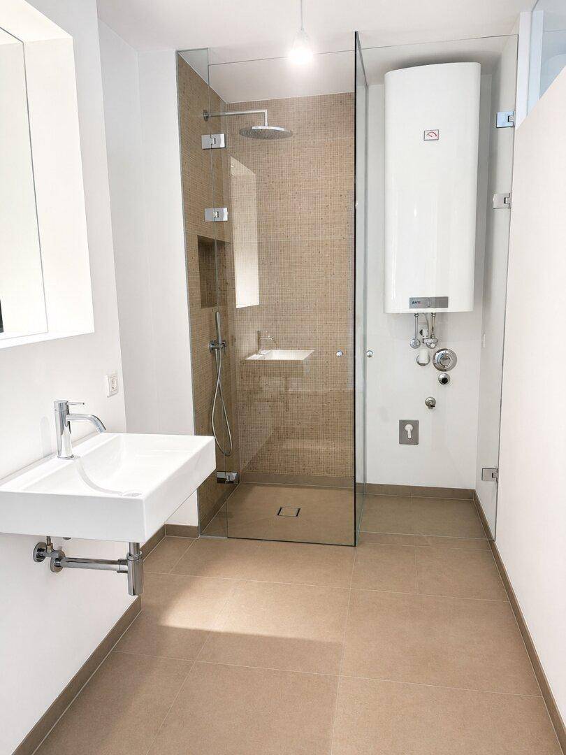 Modernes Badezimmer mit ebenerdiger Dusche, Wand-WC und großem Warmwasserboiler.