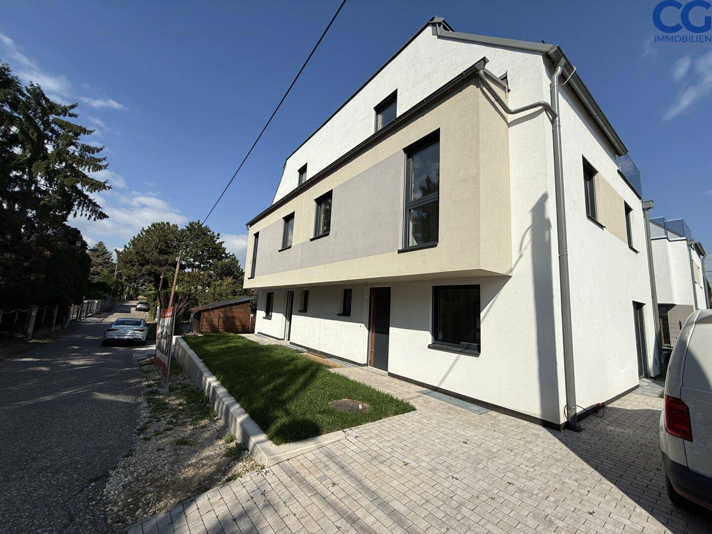 Seitenansicht einer modernen Doppelhaushälfte mit gepflastertem Zugang und angrenzender Straße.