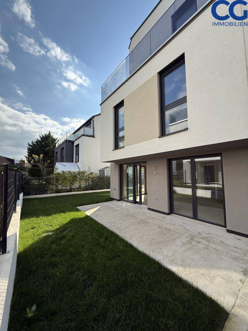 Sonniger Terrassenbereich mit direktem Zugang zum Garten und Blick auf die moderne Fassade.