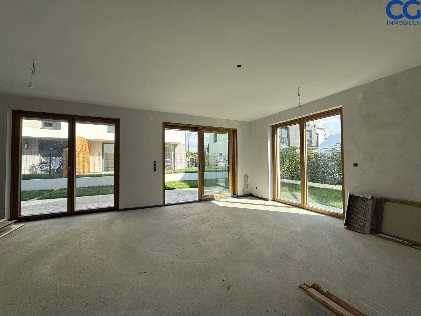 Geräumiger, unfertiger Wohnbereich mit großen Fenstern und Terrassenzugang, bereit für den Ausbau.