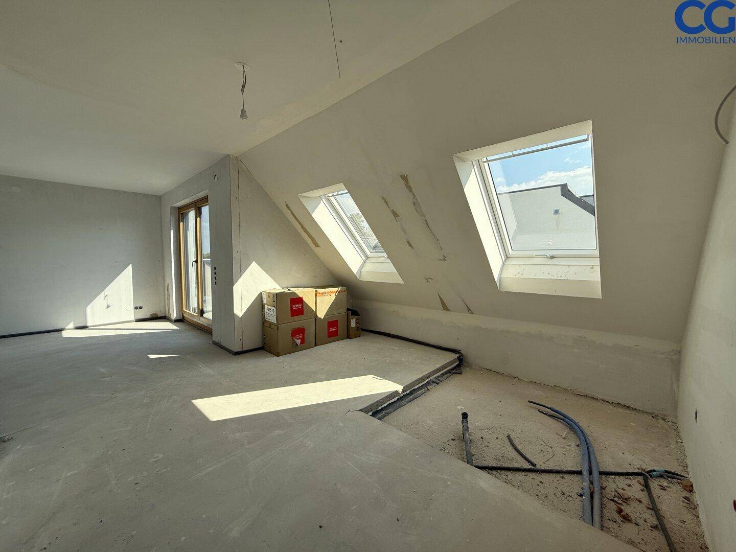 Heller Dachgeschossraum im Rohbau mit schrägen Wänden und mehreren Dachfenstern für viel Licht.