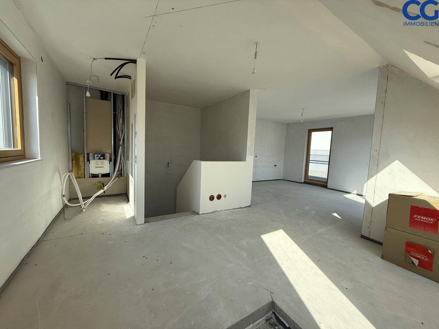 Großer Rohbauraum mit Treppenaufgang und sichtbaren Installationen, wartet auf Fertigstellung.