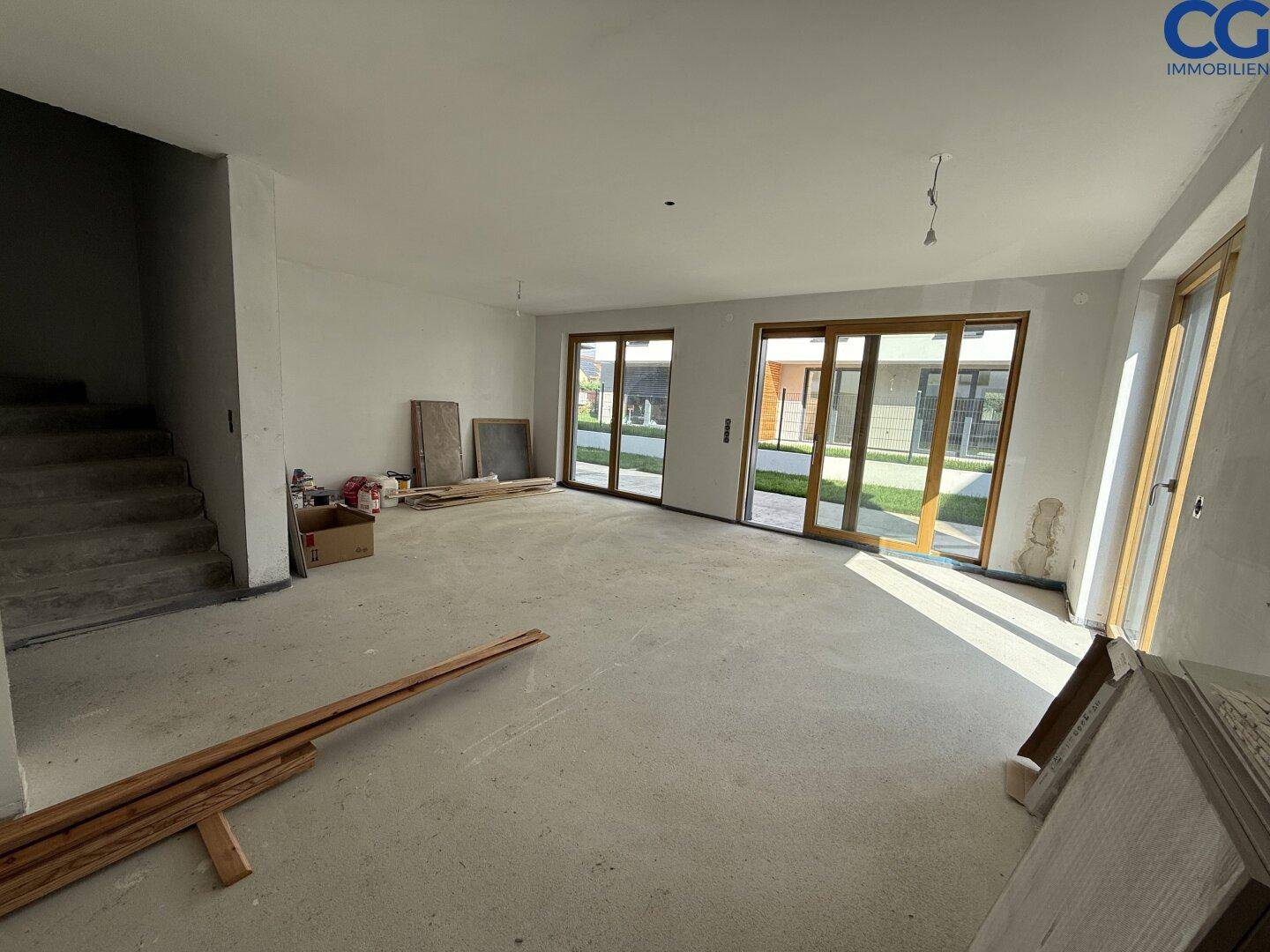 Geräumiger Wohnbereich im Rohbau mit großen Fensterfronten und Zugang zum Außenbereich.