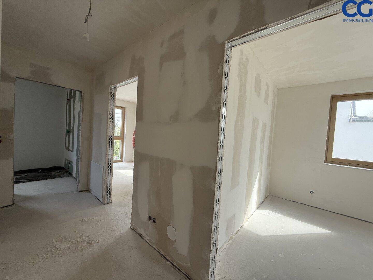 Flurbereich im Rohbau mit Türöffnungen zu angrenzenden Räumen, bereit für den Innenausbau.