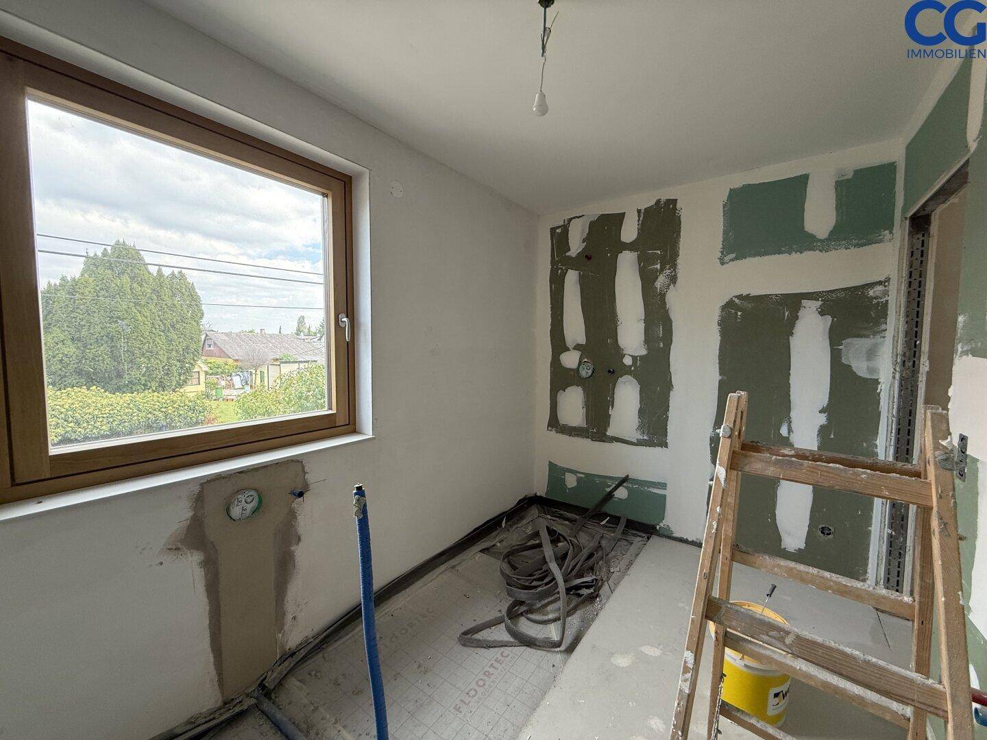 Badezimmer im Rohbau mit sichtbaren Wasseranschlüssen und Fenster, bereit für die Installation.