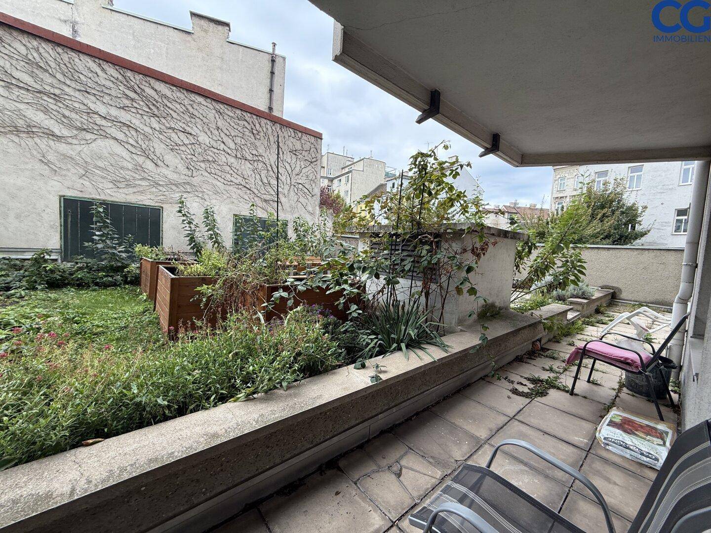 Eine begrünte Terrasse mit Pflanzenbeeten und Sitzgelegenheiten, umgeben von Gebäuden.