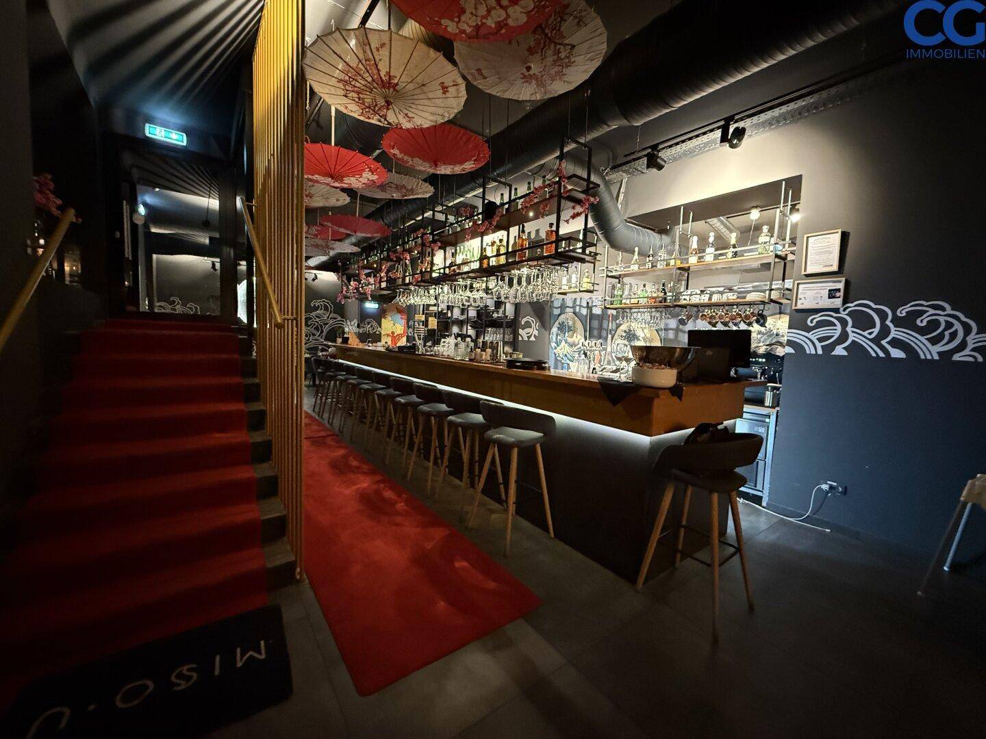 Stilvoller Barbereich mit rotem Teppich und Treppe, umgeben von dunklen Wänden und japanischer Dekoration.