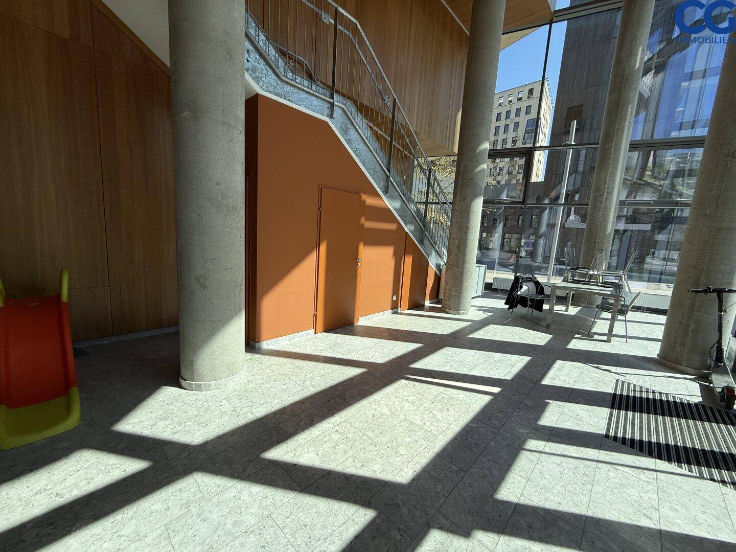 Heller Eingangsbereich eines modernen Gebäudes mit Treppe und großen Glasflächen.