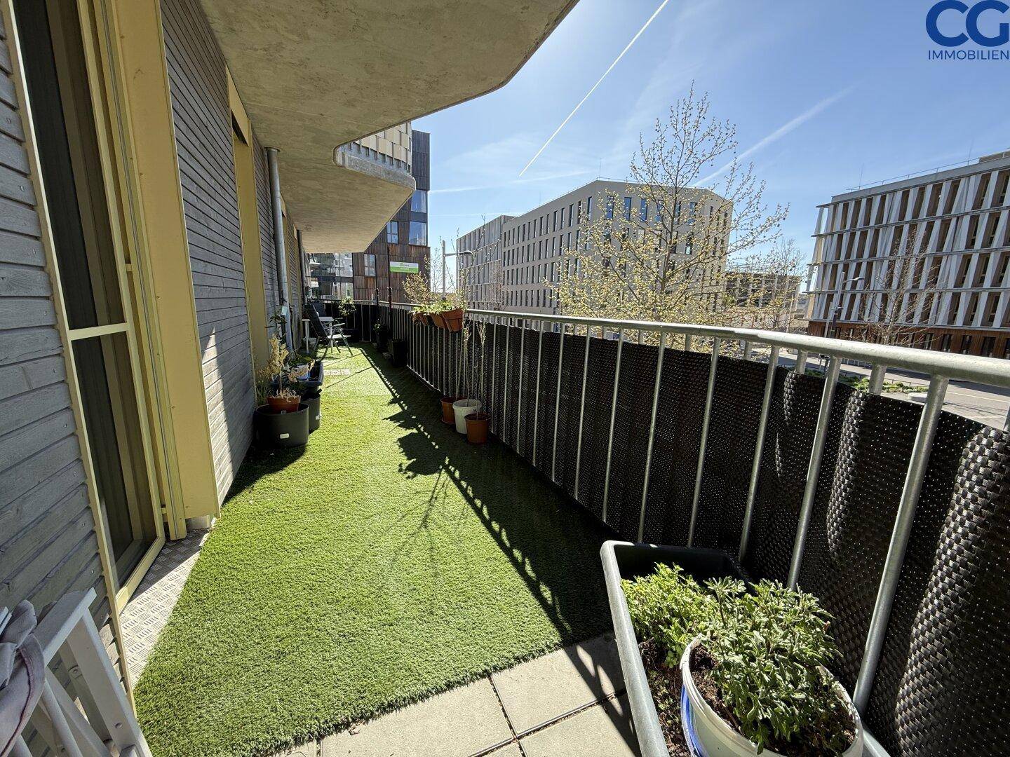 Sonniger Balkon mit Kunstrasen und seitlichem Blick auf die moderne Gebäudearchitektur.