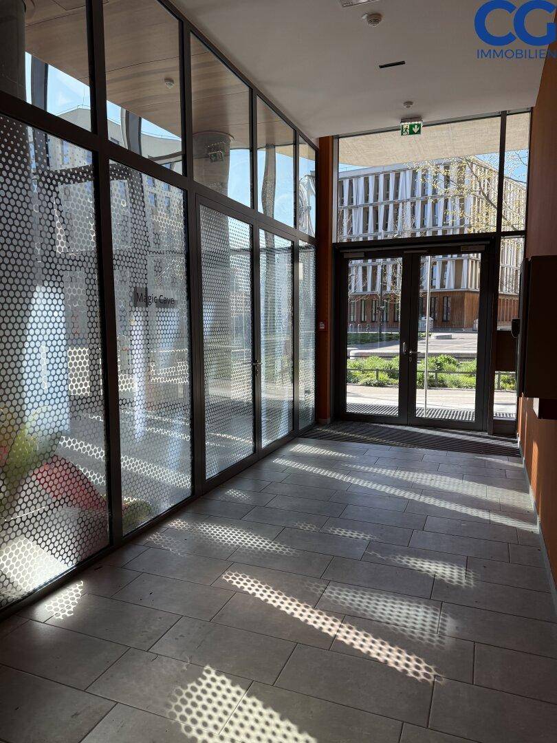Heller Eingangsbereich mit großen Glaswänden und Blick ins Freie durch die Haupttüren.