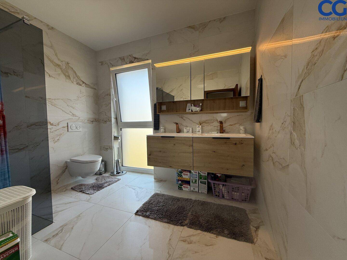 Modernes Badezimmer mit Marmorfliesen, Doppelwaschbecken und wandhängendem WC.