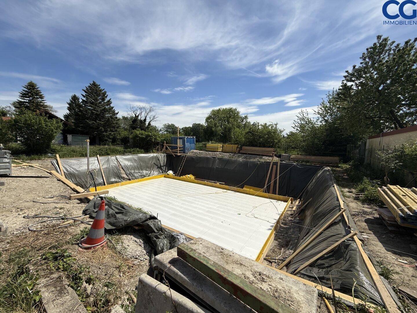 Baustelle mit vorbereitetem Fundament für ein neues Gebäude unter blauem Himmel.