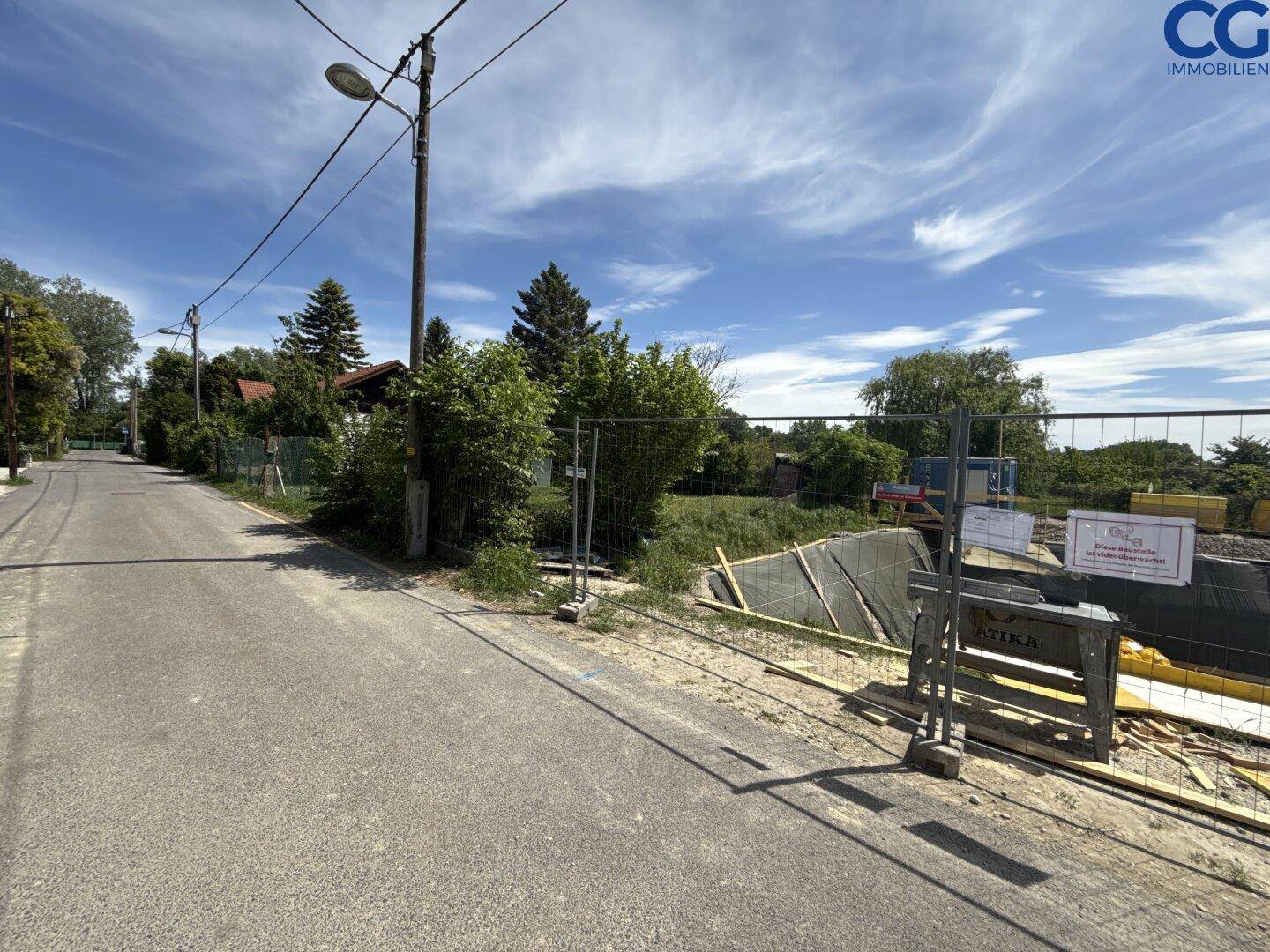 Blick auf eine ruhige Straße neben einer Baustelle mit Bauzaun und Vegetation.