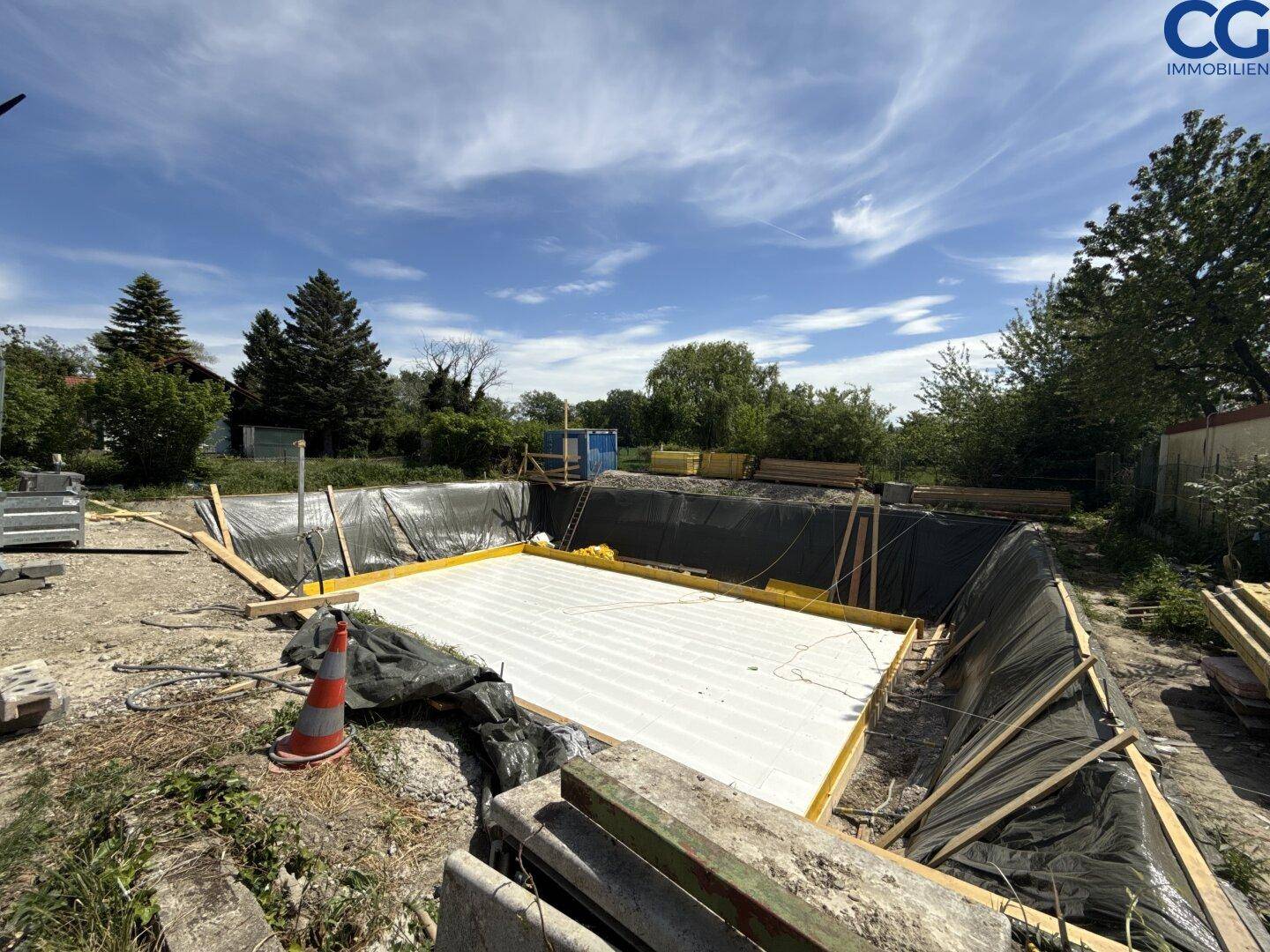 Baugrube für ein neues Fundament mit bereits verlegter Isolierung unter blauem Himmel.