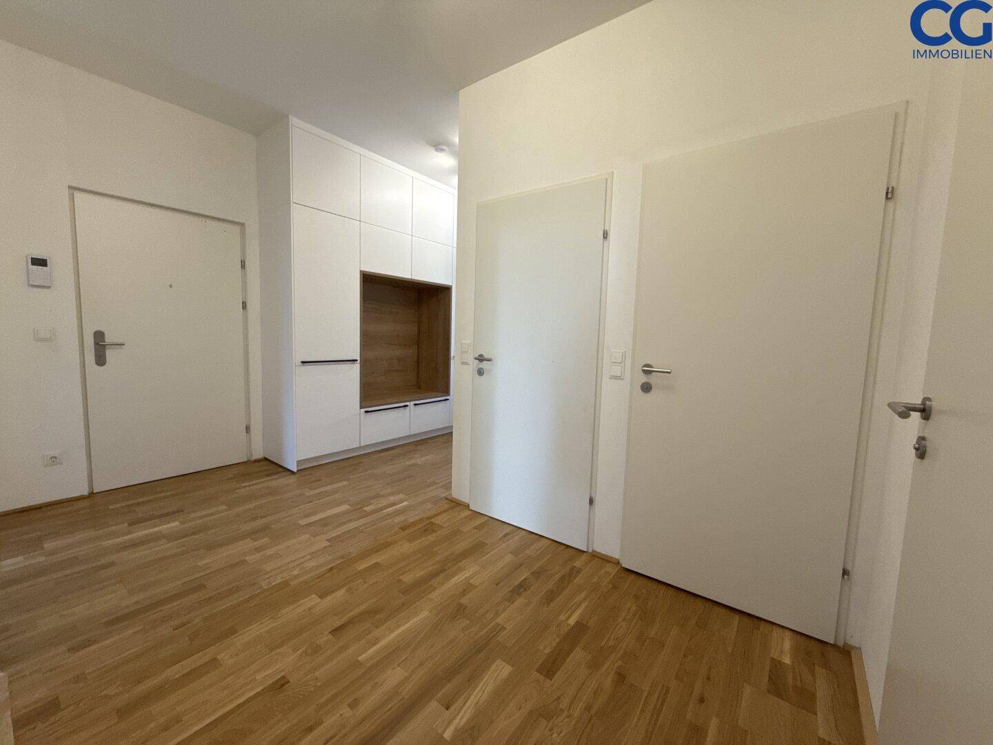 Geräumiger Flur mit mehreren Türen und praktischen weißen Einbauschränken, auf Holzboden.