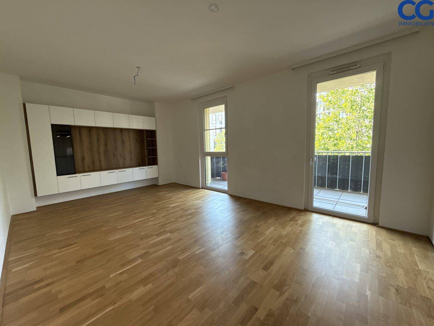 Heller, leerer Wohnraum mit Holzboden und zwei Balkonzugängen, bereit zur individuellen Gestaltung.