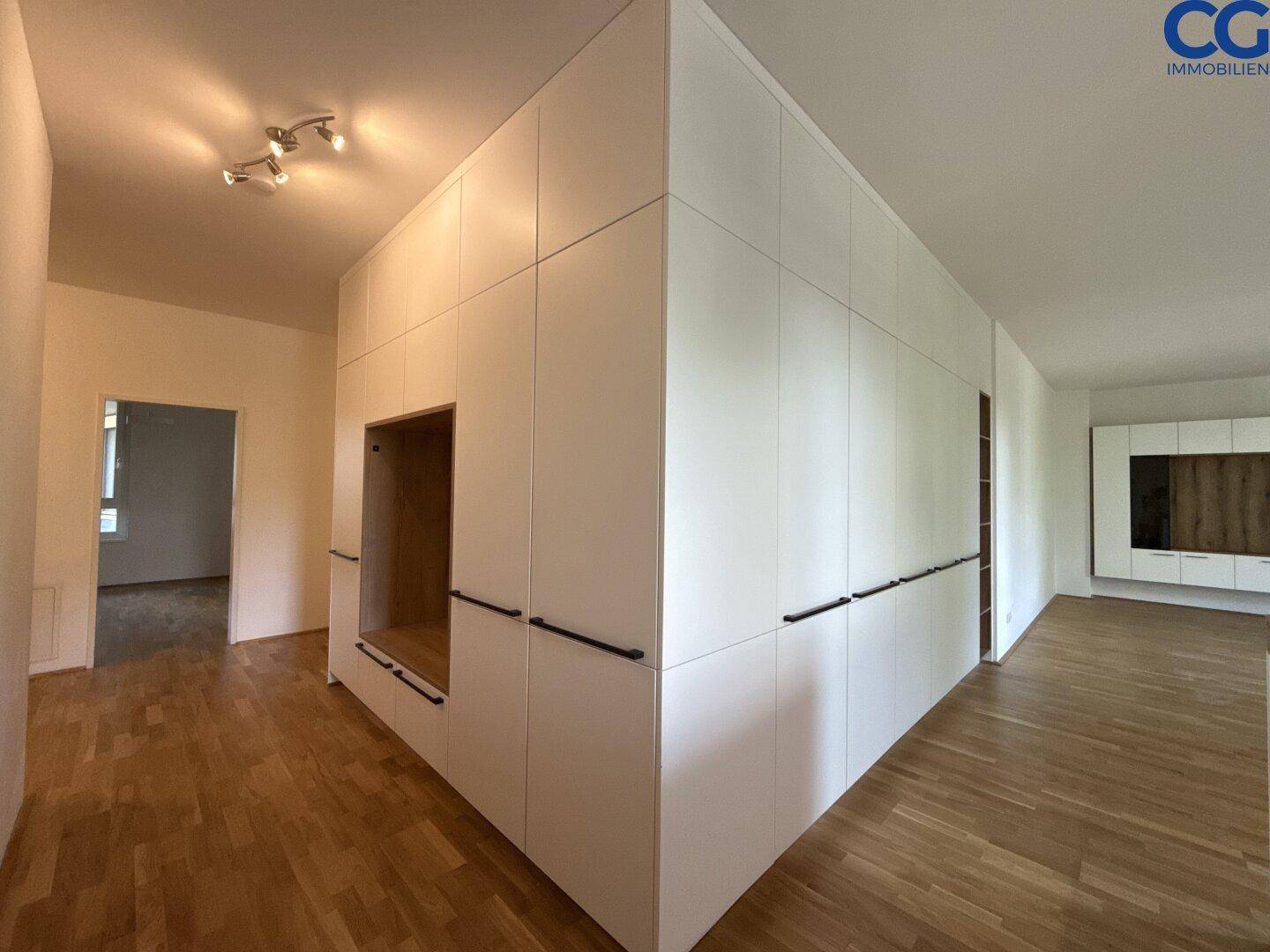 Heller Flur mit integrierten weißen Schränken und Holzboden, der zu weiteren Räumen führt.