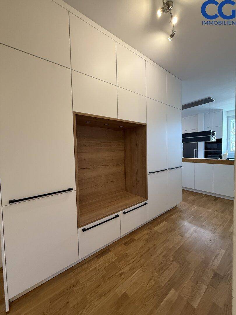 Eingangsbereich mit modernen weißen Einbauschränken und Holzboden, mit Blick zur Küche.