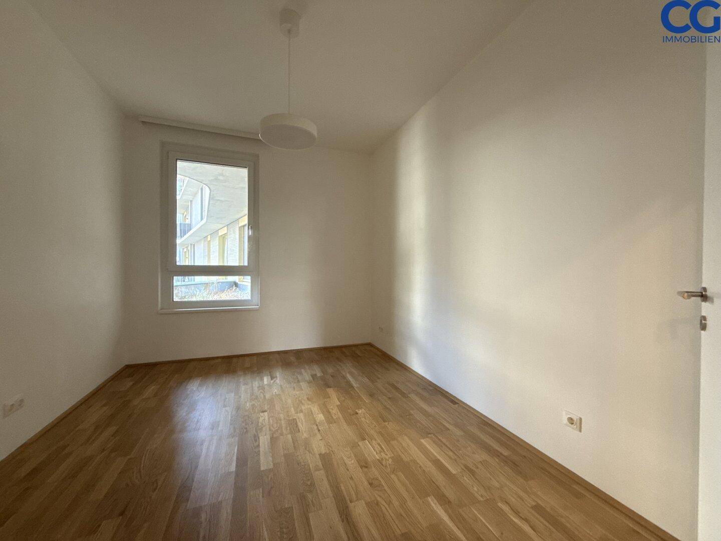 Leeres Zimmer mit Holzboden und einem Fenster, ideal als Schlaf- oder Arbeitszimmer nutzbar.