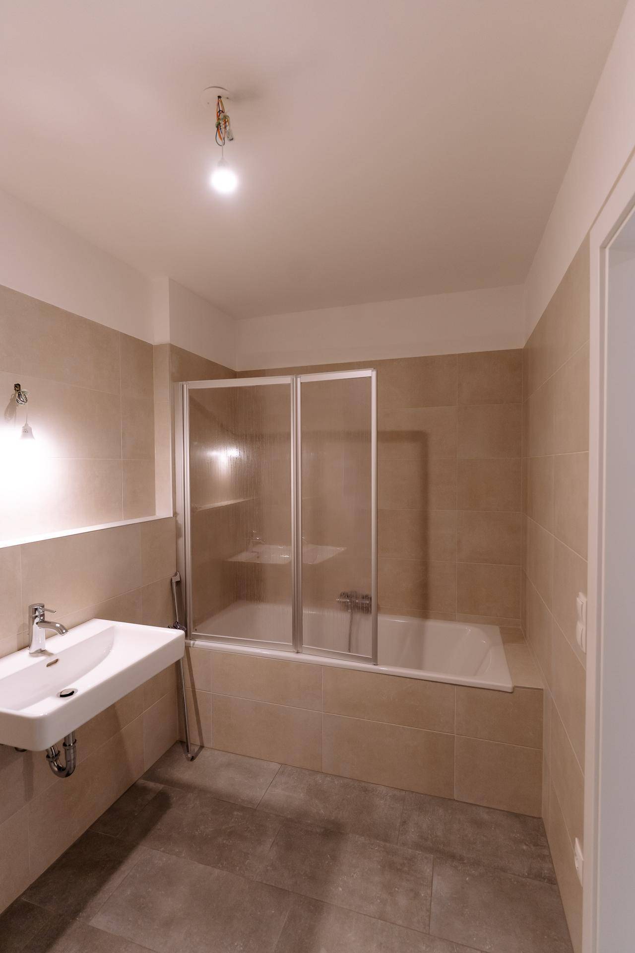 Modernes Badezimmer mit Badewanne, Duschabtrennung und beigefarbenen Fliesen.