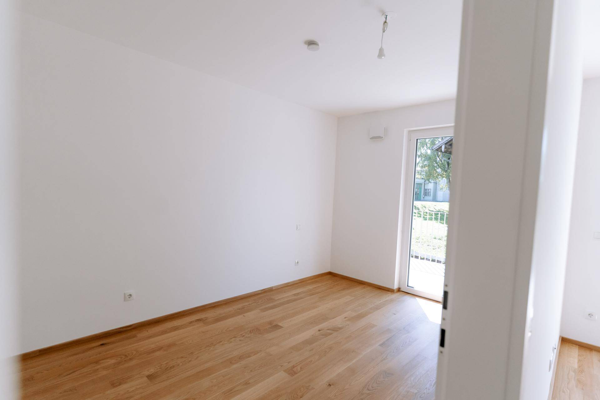 Lichtdurchfluteter Raum mit Parkettboden und Zugang zum Außenbereich, perfekt für individuelle Gestaltung.