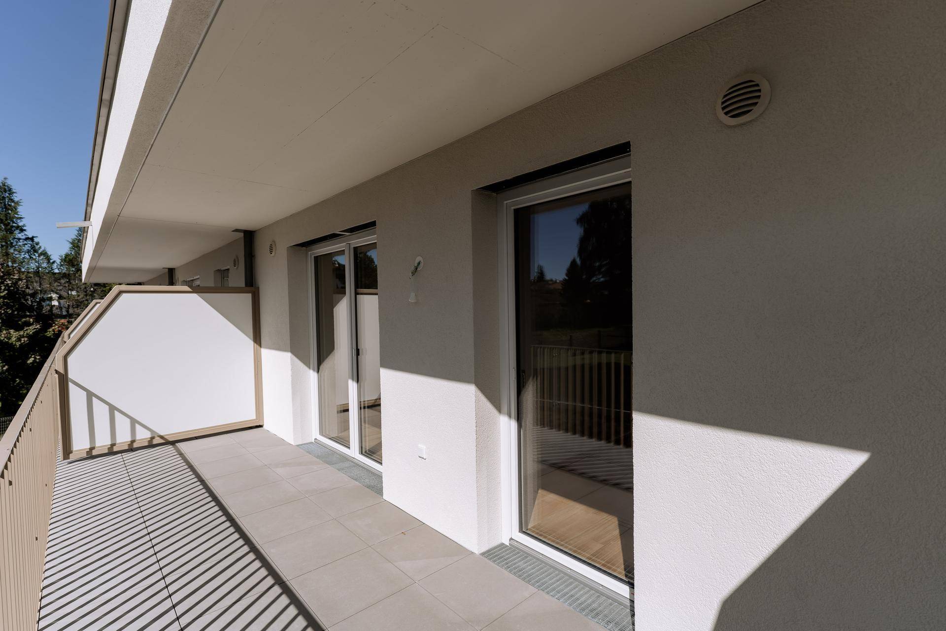 Langer, sonniger Balkon mit Fliesenboden und moderner Brüstung, ideal zum Entspannen im Freien.