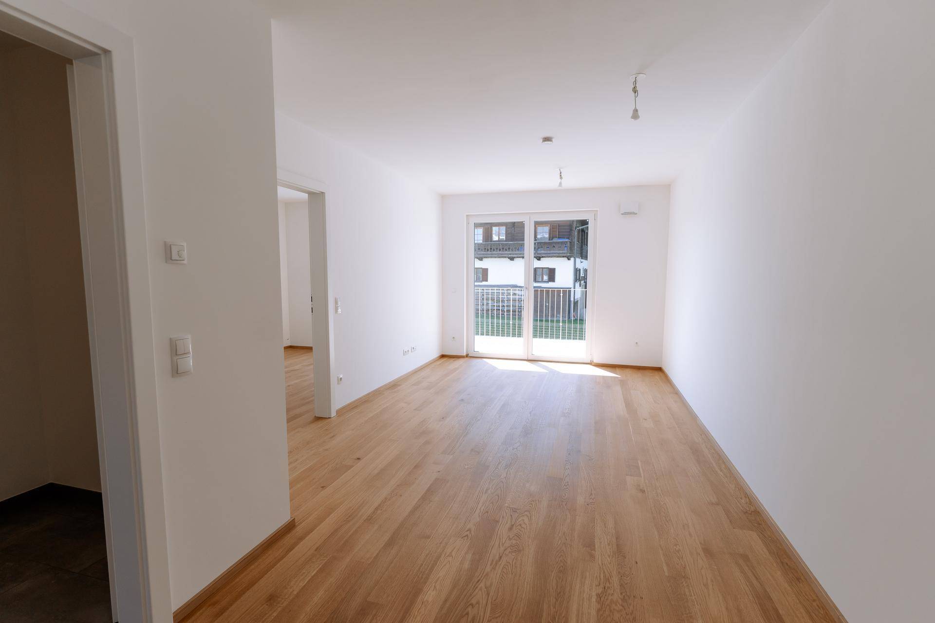 Geräumiges Zimmer mit hellem Parkettboden und großem Fenster mit Blick auf die Umgebung.