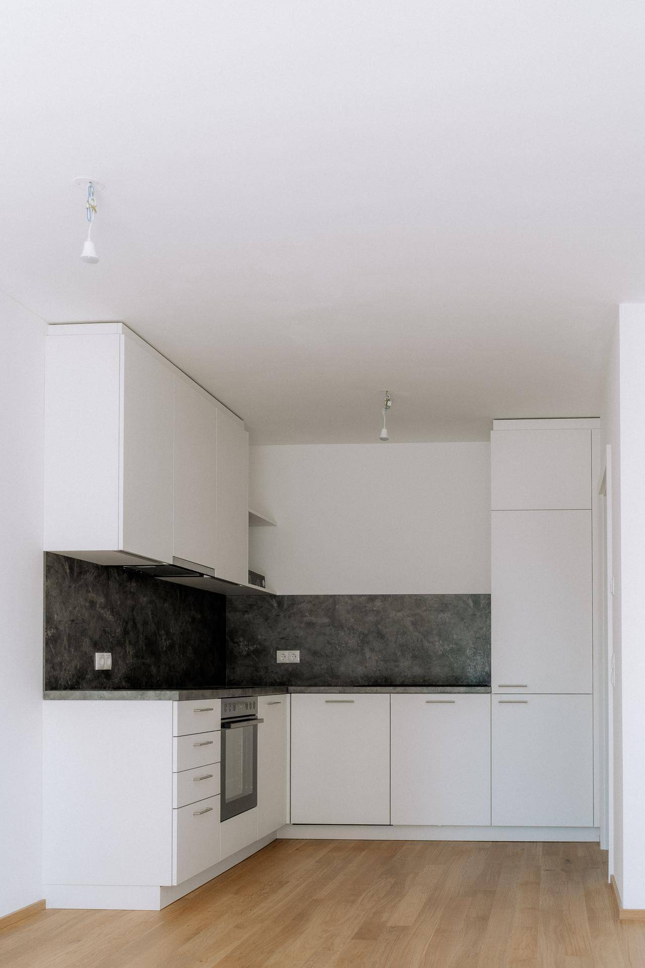 Moderne Einbauküche mit weißen Schränken, dunkler Arbeitsplatte und integriertem Backofen.