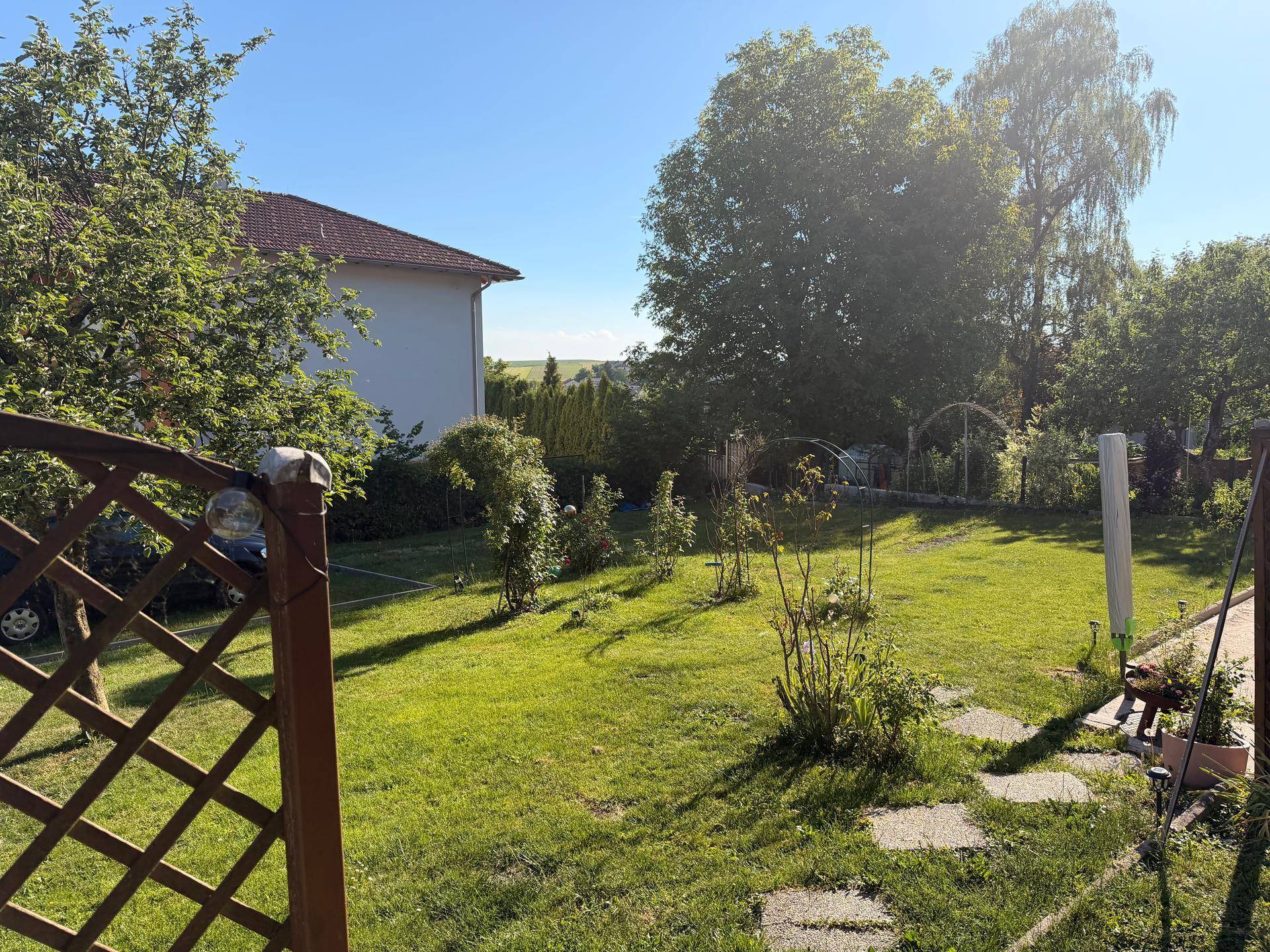 Sonniger Garten mit Rasenfläche, Bäumen und Blick auf die umliegende Landschaft.