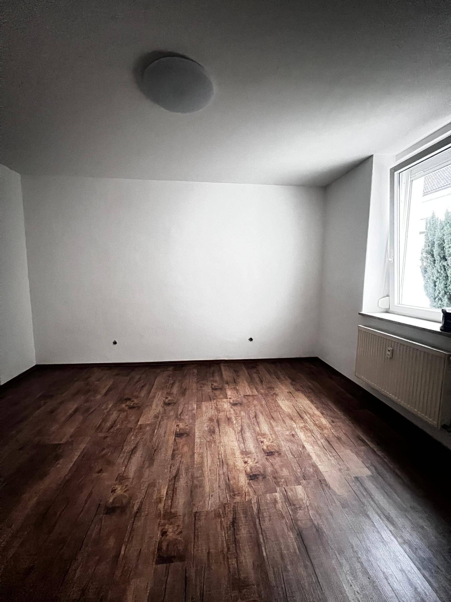 Geräumiges Zimmer mit Laminatboden in Holzoptik und großem Fenster, ideal als Schlafzimmer.
