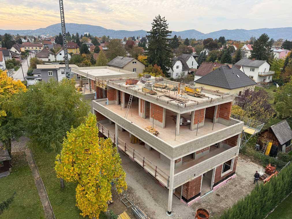 Neubauprojekt im Bauzustand, umgeben von grüner Landschaft und anderen Wohnhäusern.