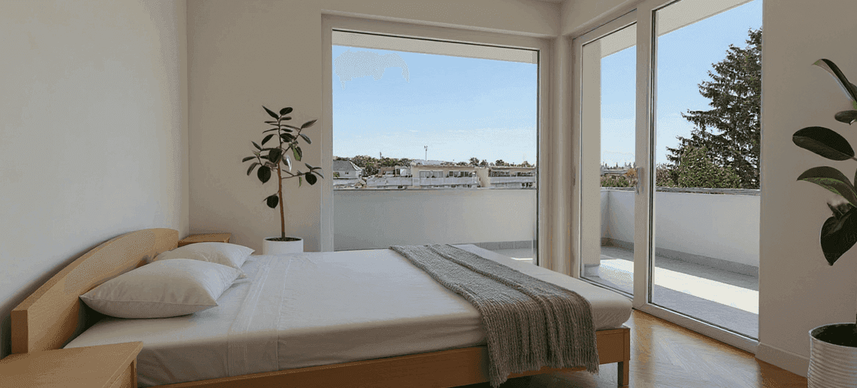 Schlafzimmer mit Holzbett, großen Fenstern und Zugang zu einem Balkon.