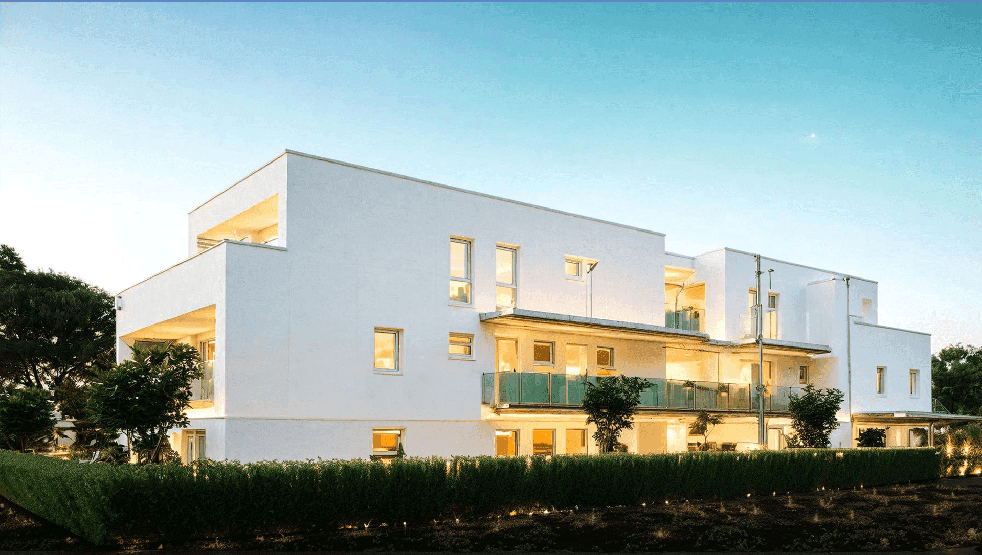 Moderne Wohnanlage mit weißer Fassade, großen Fenstern und gepflegter Hecke.