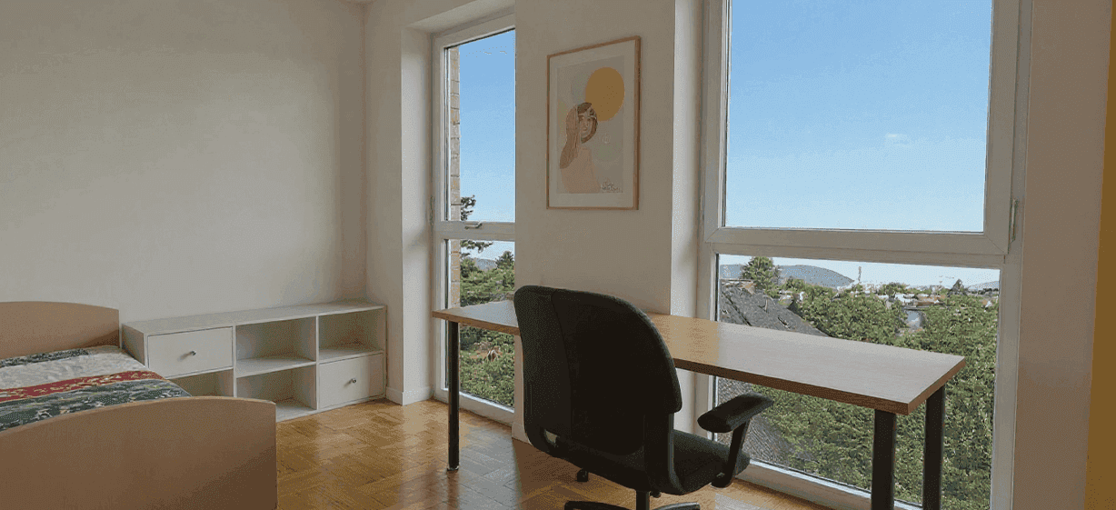 Arbeitszimmer mit großem Fenster, Schreibtisch und Blick ins Grüne.