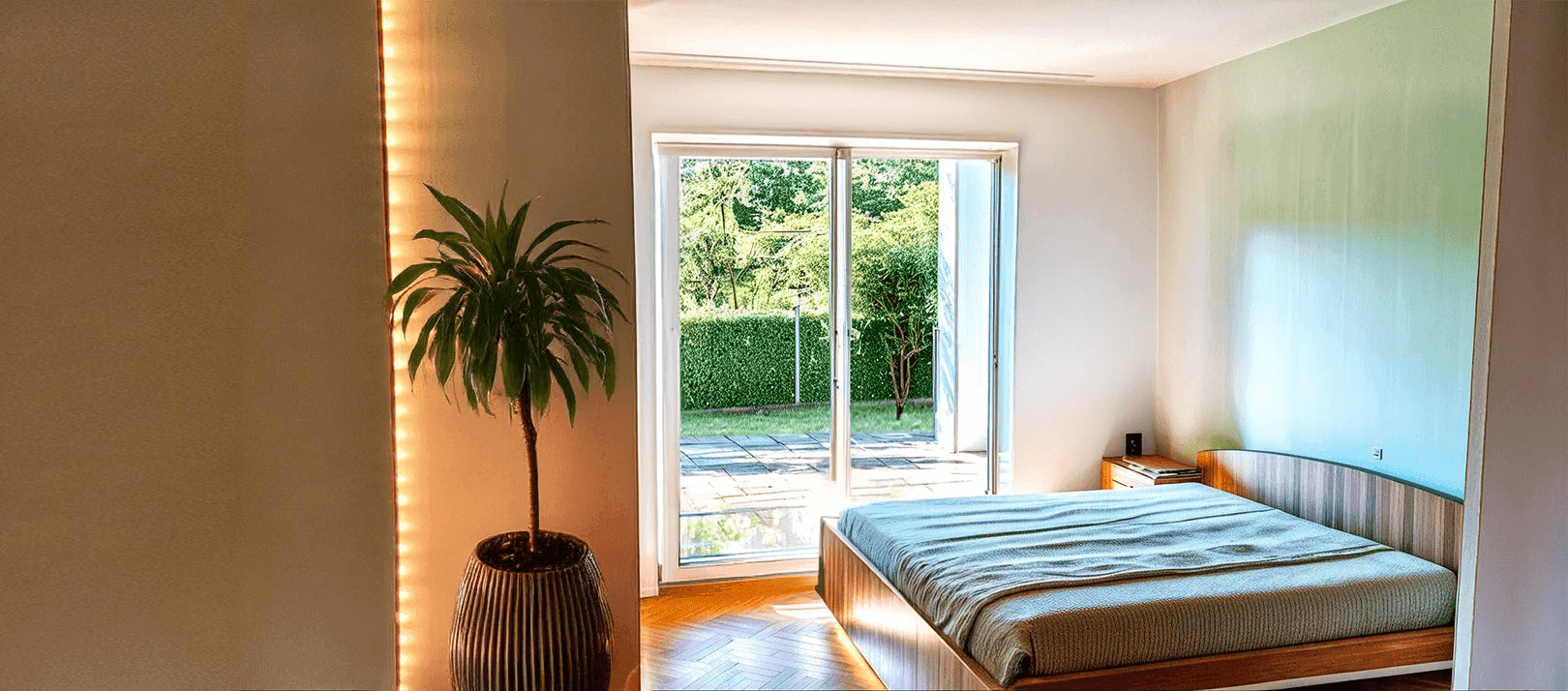Helles Schlafzimmer mit Holzboden, Zugang zum Garten und einer dekorativen Pflanze.