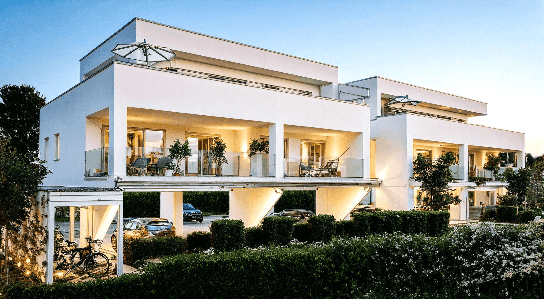 Moderne Wohnanlage mit Carports, Balkonen und gepflegten Grünflächen am Abend.