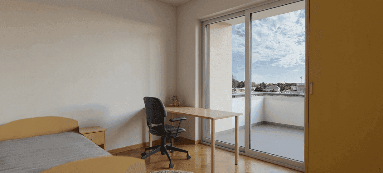 Helles Arbeitszimmer mit Schreibtisch, Bürostuhl und Zugang zu einem Balkon.