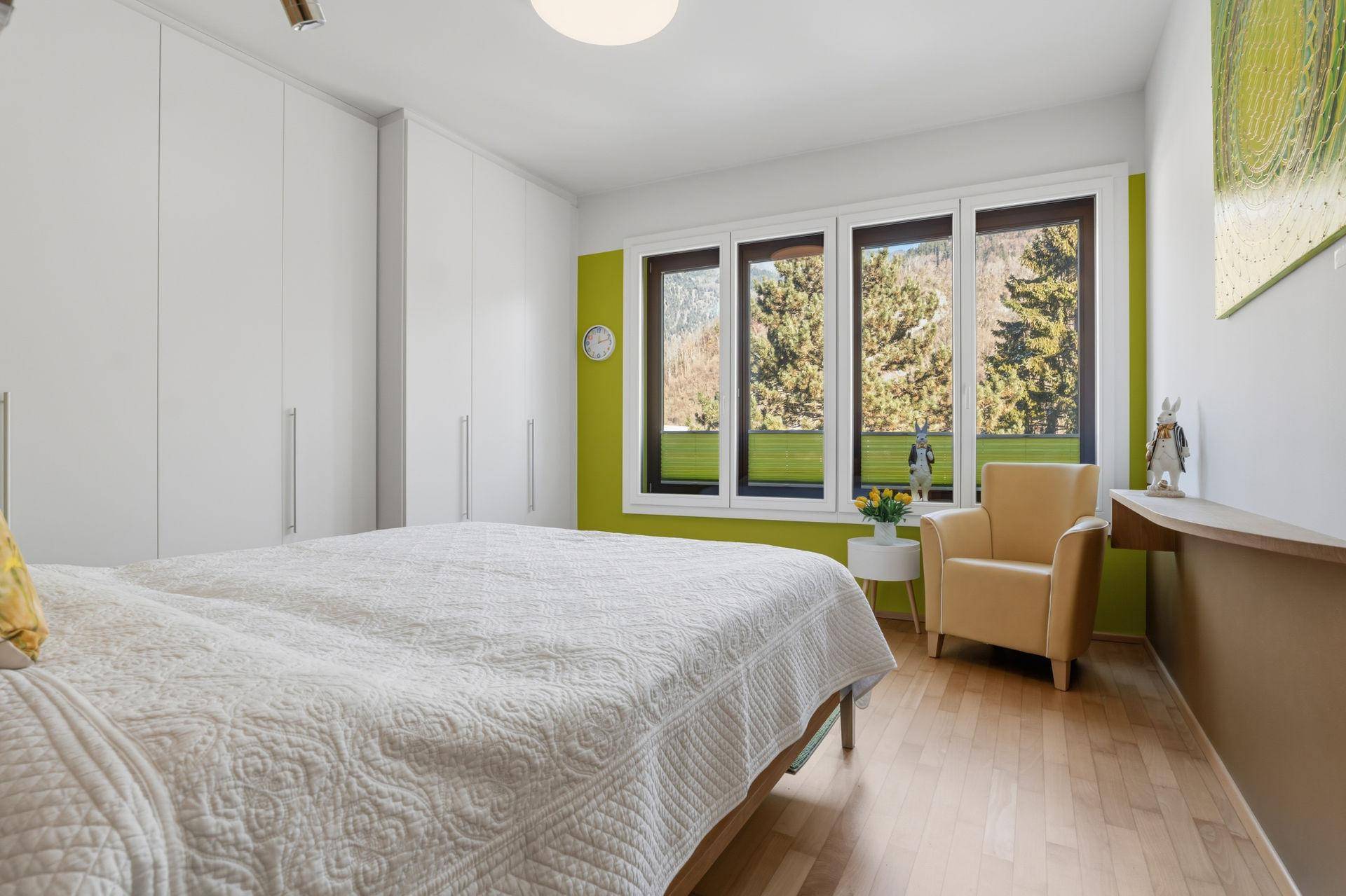 Schlafzimmer mit großen Fenstern, Einbauschränken und Blick ins Grüne.