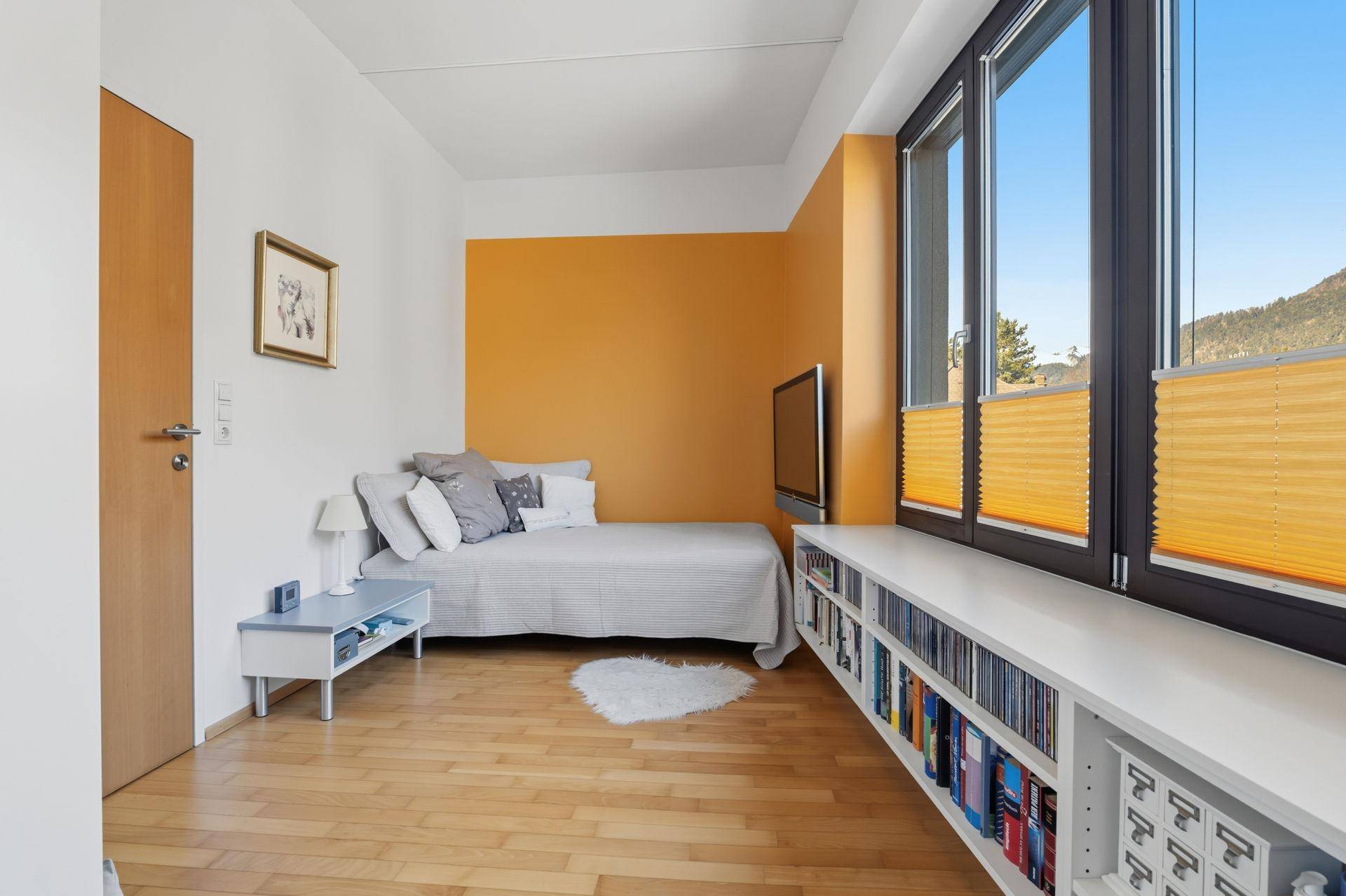 Helles Schlafzimmer mit Einzelbett, Wandfernseher und Fenster mit Ausblick.