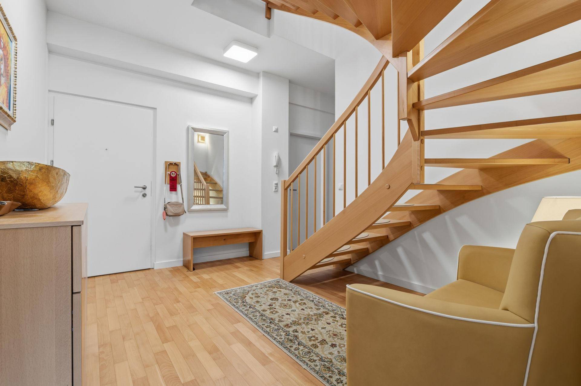 Heller Eingangsbereich mit eleganter Holzwendeltreppe, Sitzbank und Parkettboden.