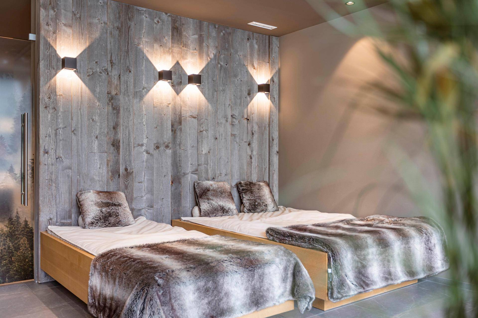 Schlafzimmer mit zwei Einzelbetten, einer Holzwand und flauschigen Decken für eine warme Atmosphäre.