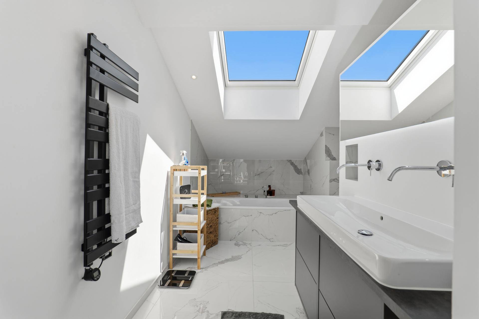 Modernes Badezimmer im Dachgeschoss mit Badewanne, Waschbecken, Handtuchheizkörper und Dachfenster.