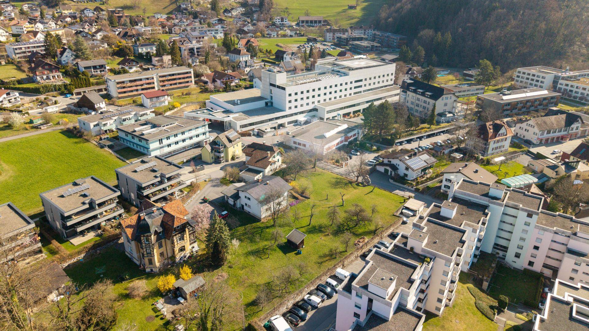 Weitläufige Luftaufnahme einer Stadt mit Wohngebäuden, Grünflächen und einem Krankenhauskomplex.