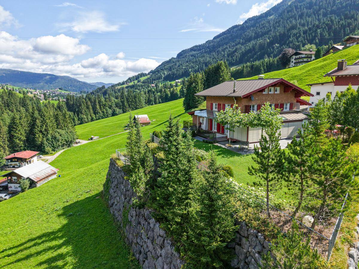 Alpines Haus auf einem Hügel mit weitem Blick über das Tal und grüne Wiesen.