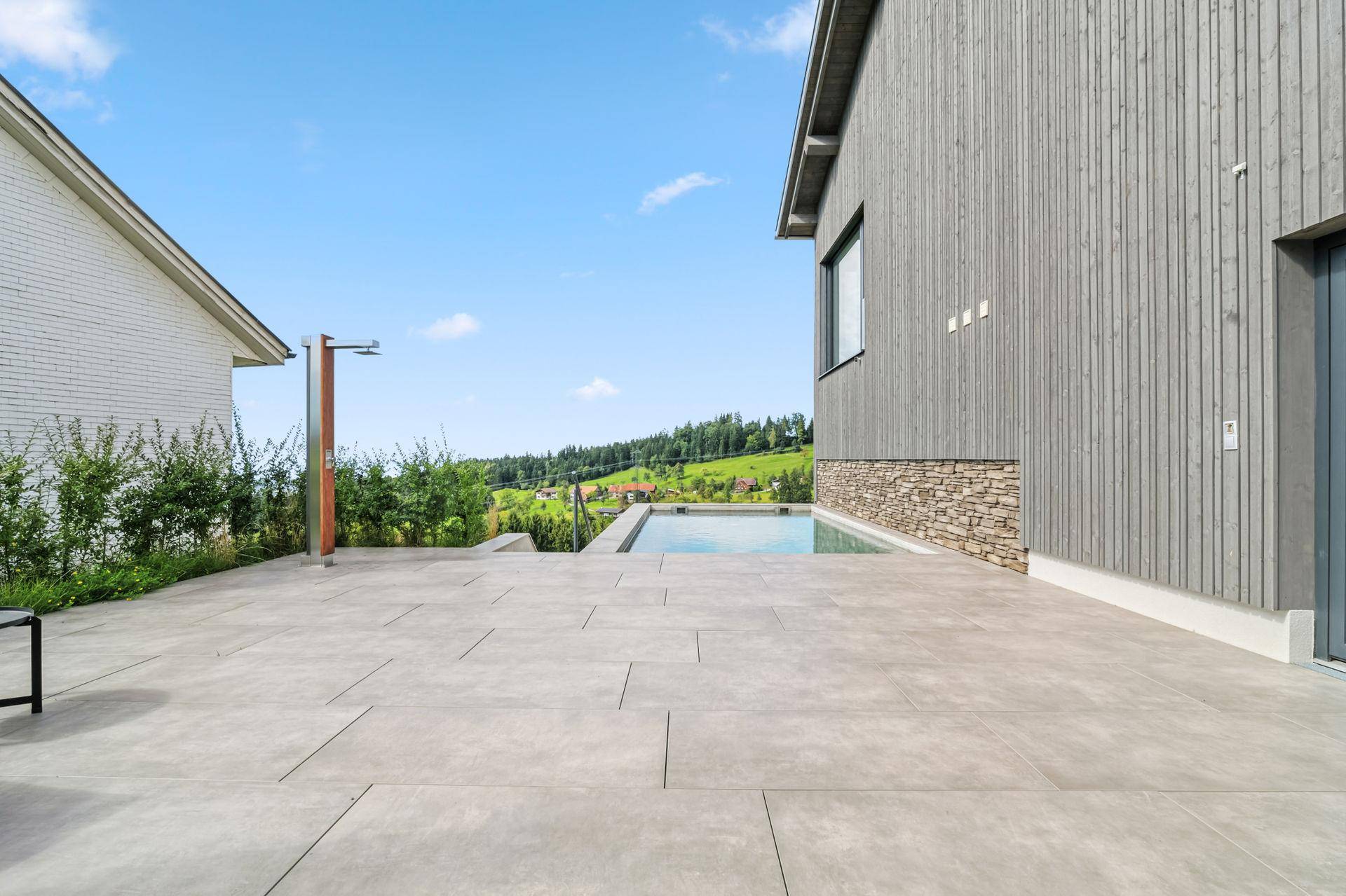 Große Außenterrasse mit kleinem Pool, Fliesenboden und Blick auf die grünen Hügel.