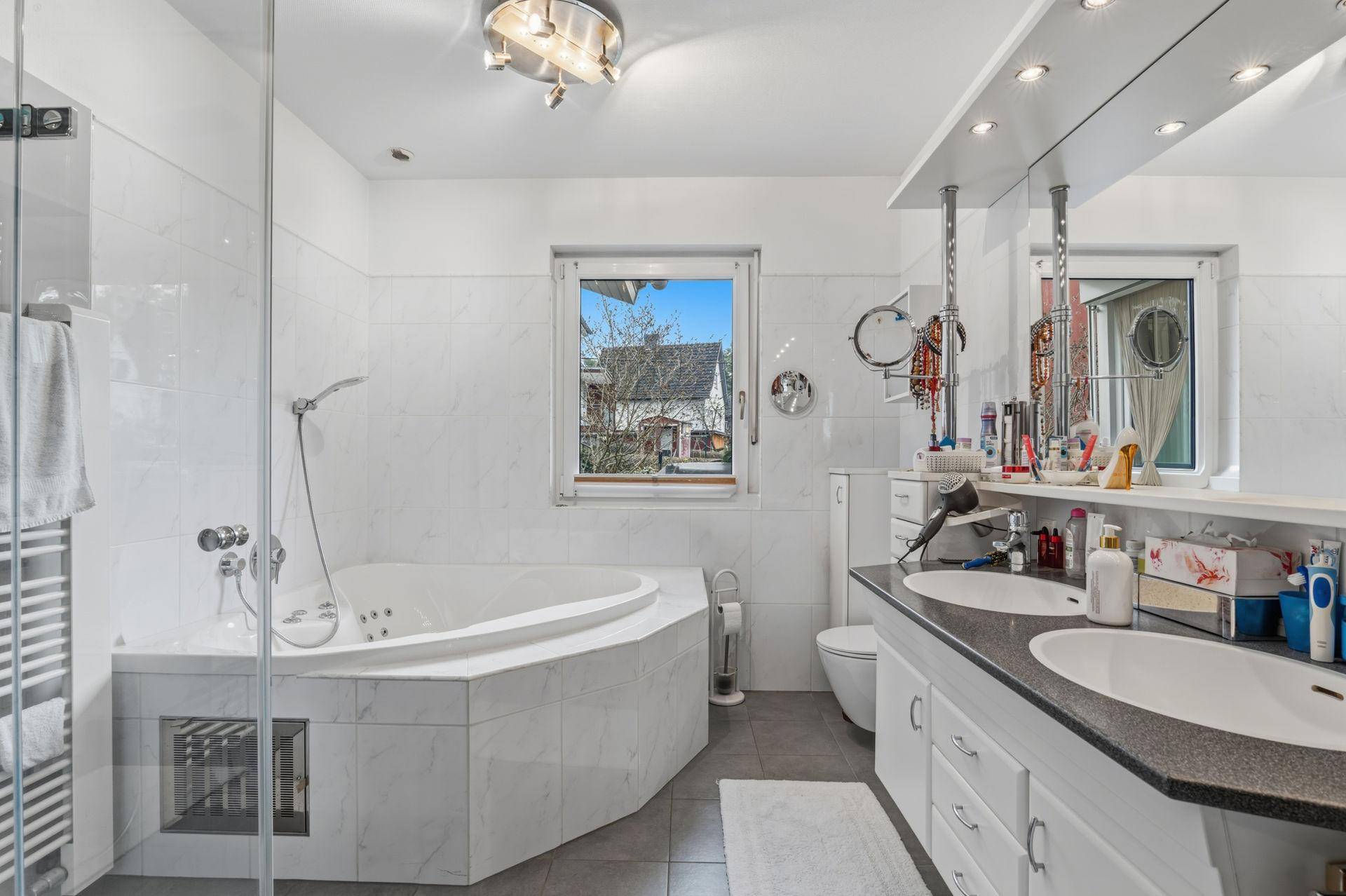 Modernes Badezimmer mit Eckbadewanne, Doppelwaschbecken und Fenster für Tageslicht.