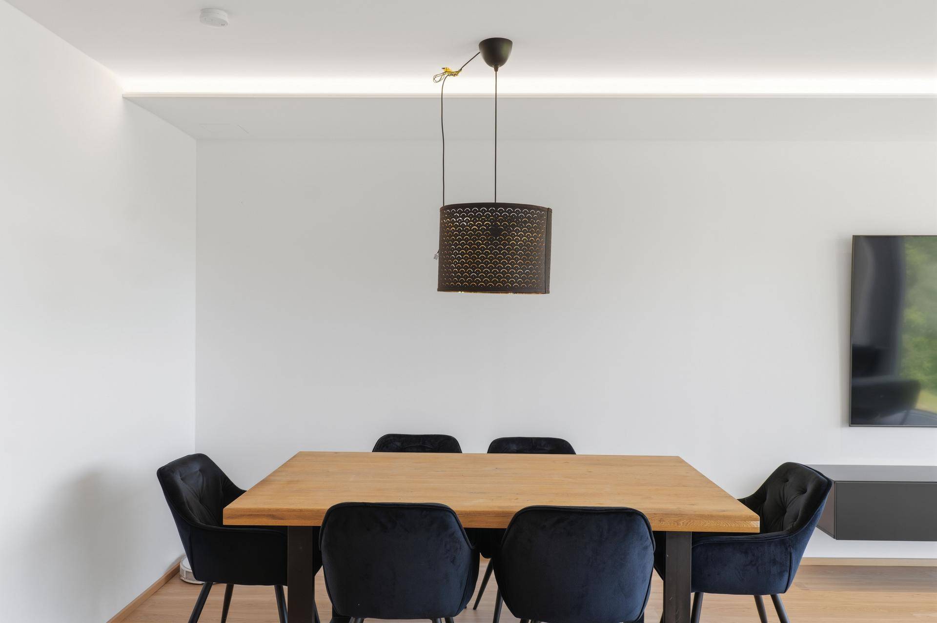 Eleganter Essbereich mit massivem Holztisch, Samtstühlen und moderner Hängelampe.