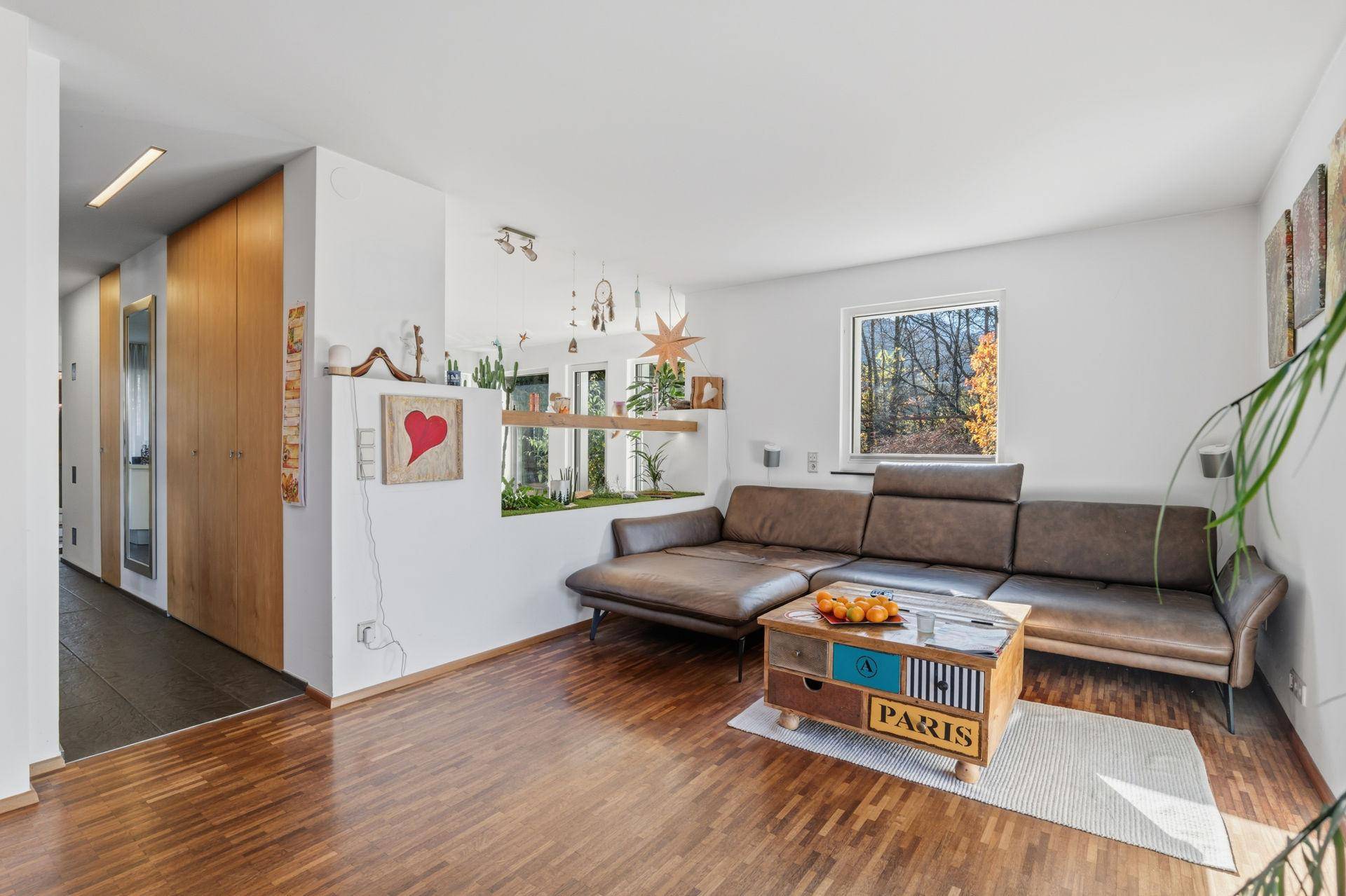 Gemütliches Wohnzimmer mit braunem Ecksofa, Holzboden und kreativer Dekoration, bietet viel Platz.