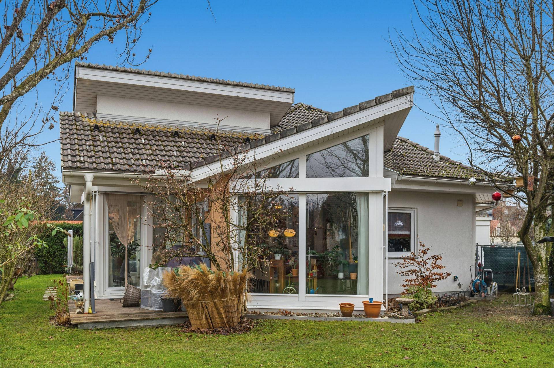 Außenansicht des Hauses vom Garten aus mit großen Fenstern und kleiner Holzterrasse.