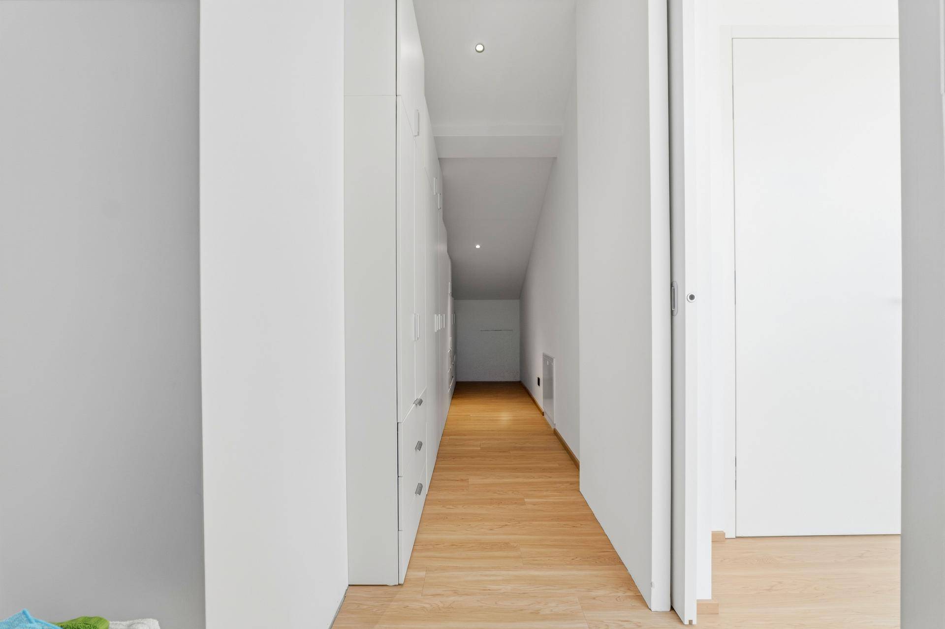 Schmaler Flur oder Abstellraum mit weißen Einbauschränken und Holzfußboden.